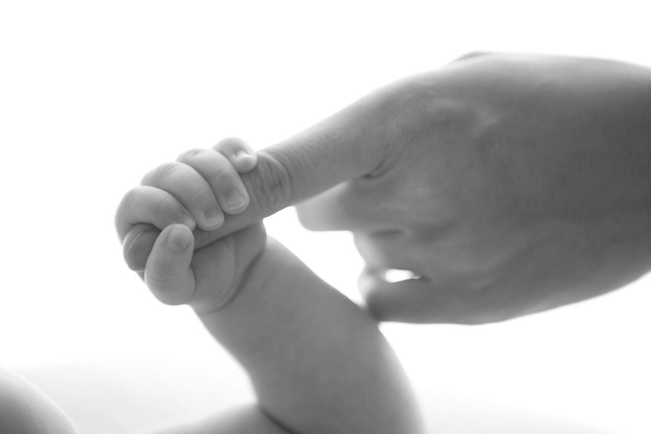 Black and white photo of a baby hand holding an adult finger.